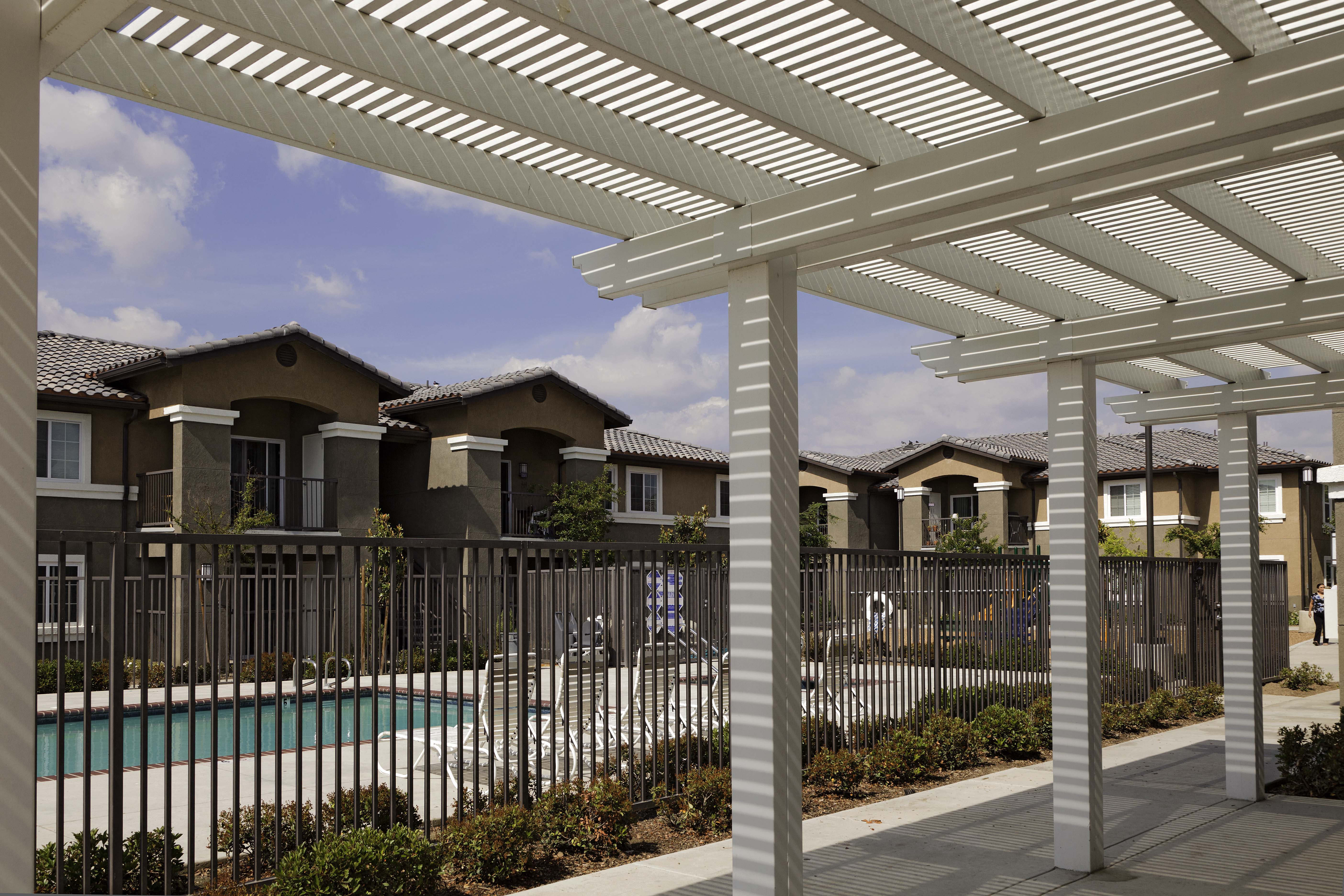 a white pergola sits in front of a pool with apartment buildings in the background