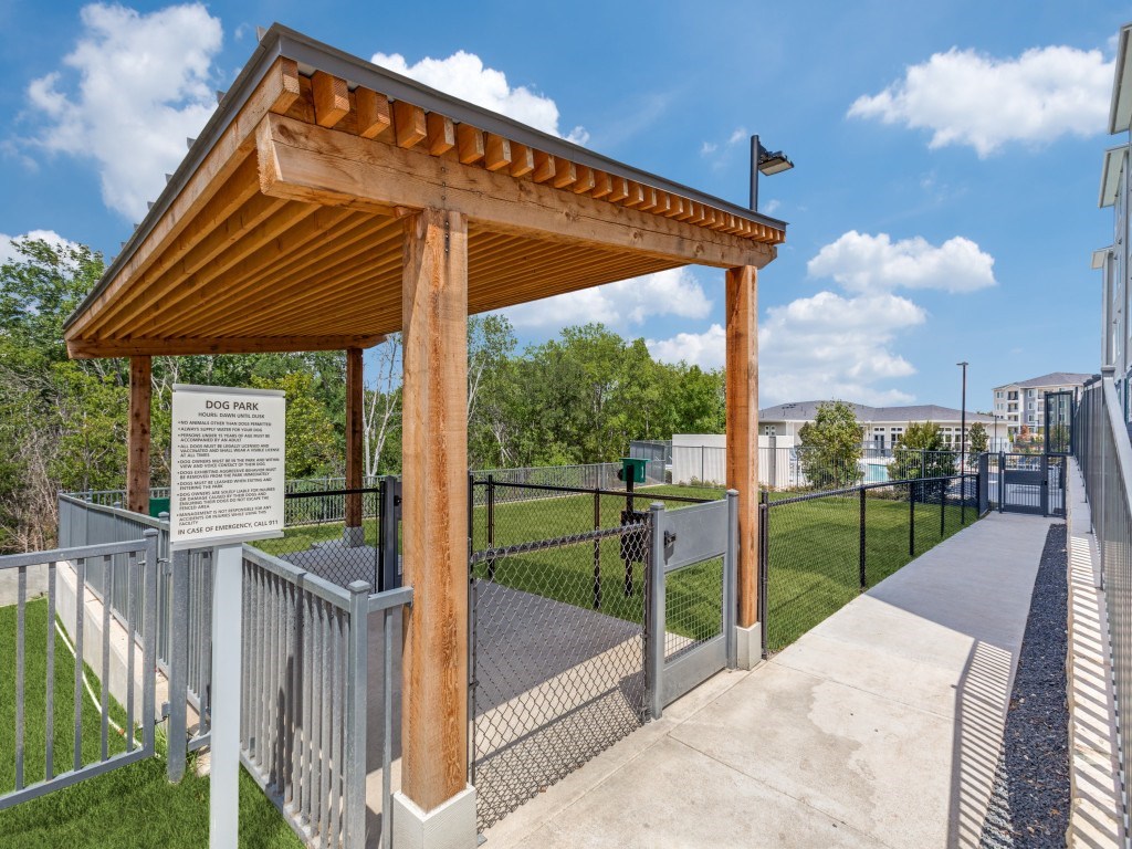 A wooden dog park shelter with a signboard and a fence.