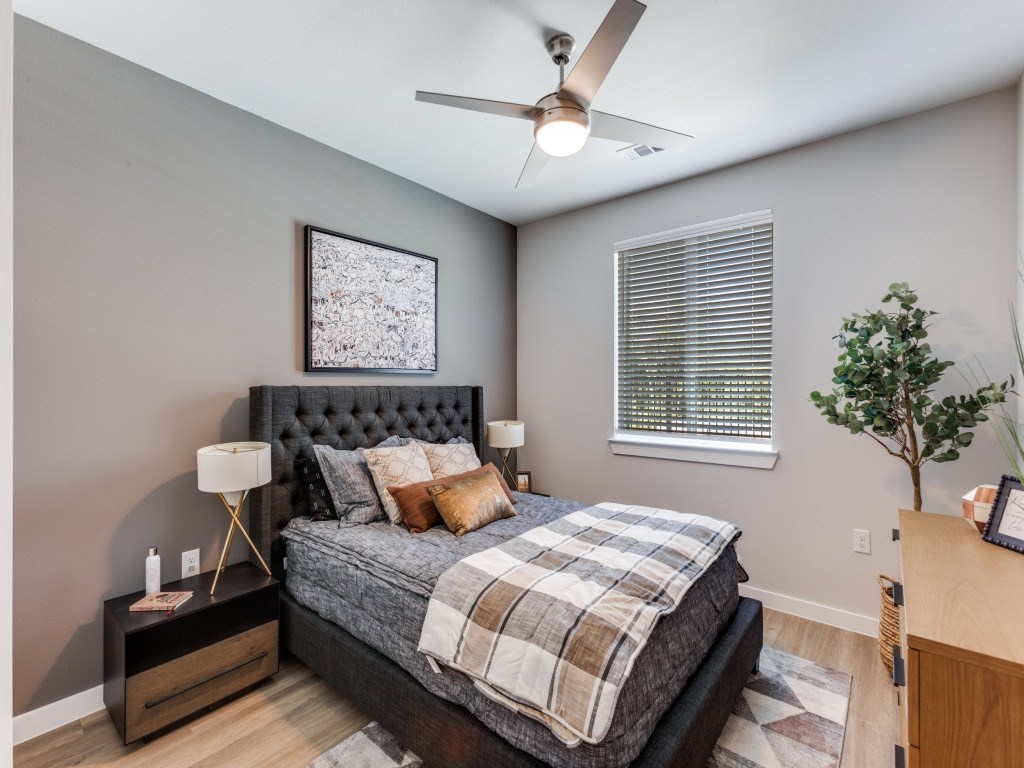 A bedroom with a bed, nightstand, and a plant.