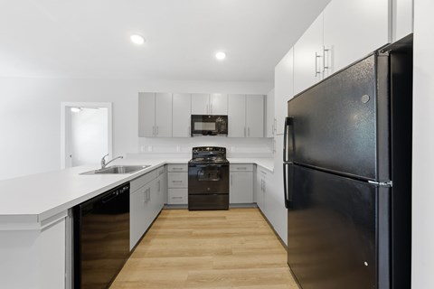 A black refrigerator is in the corner of a white kitchen.