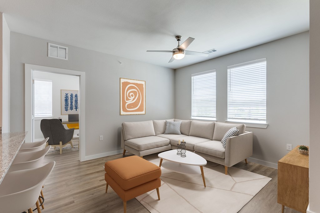 A living room with a white couch, a brown ottoman, and a ceiling fan.
