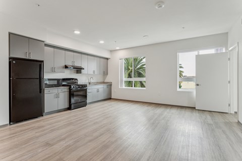 A spacious kitchen with a black refrigerator and wooden flooring.