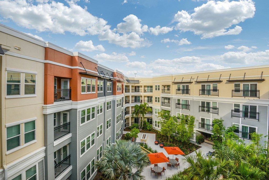 a rendering of an apartment building with trees and tables in the courtyard  at Grady Square, Tampa, 33607