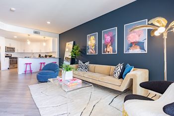 a living area with a couch coffee table and chairs and a kitchen in the background