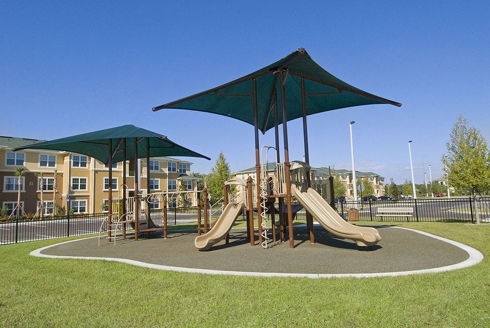 a playground with two slides and two umbrellas in front of an apartment building