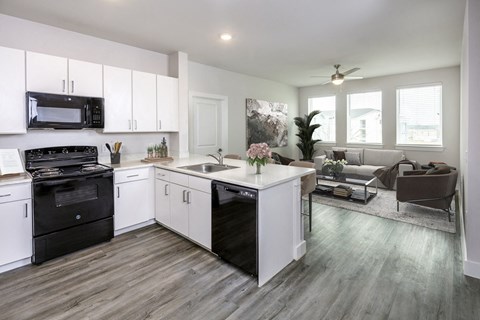 an open kitchen and living room with white cabinets and black appliances