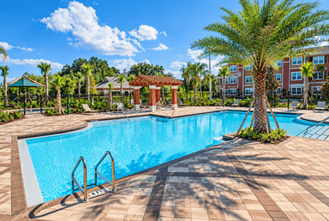 A large swimming pool surrounded by palm trees and a red gazebo.