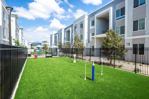 A grassy area in front of apartment buildings with a blue post and two white poles.