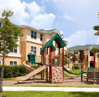 A playground with a slide and a climbing frame in front of a building.