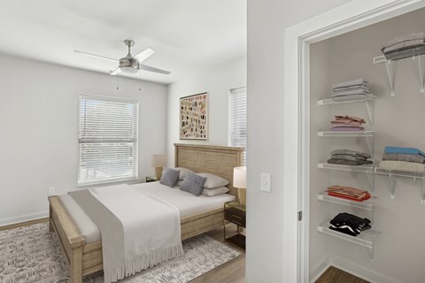 A bedroom with a bed, a fan, and a closet with clothes.