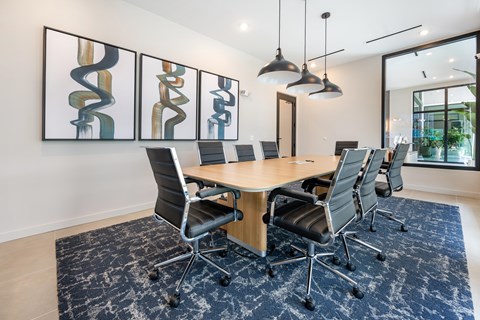 A conference room with a large table surrounded by chairs and three paintings on the wall.