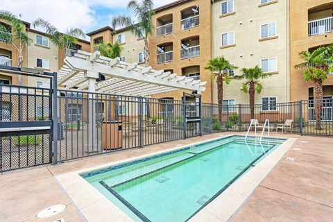 A pool surrounded by a black fence and a building in the background.