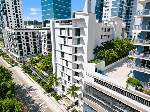 A modern white building with balconies is surrounded by other buildings.
