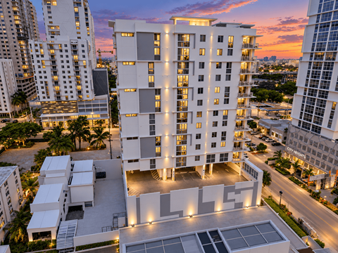 A modern white building with a glass facade is illuminated at dusk.