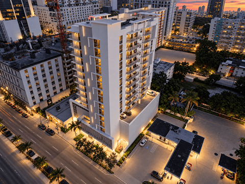 A tall white building with a parking lot in front of it.