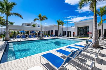 A pool surrounded by palm trees and lounge chairs.