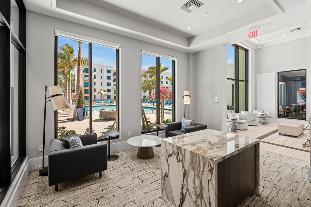 A living room with a large marble table and a view of a pool and palm trees.