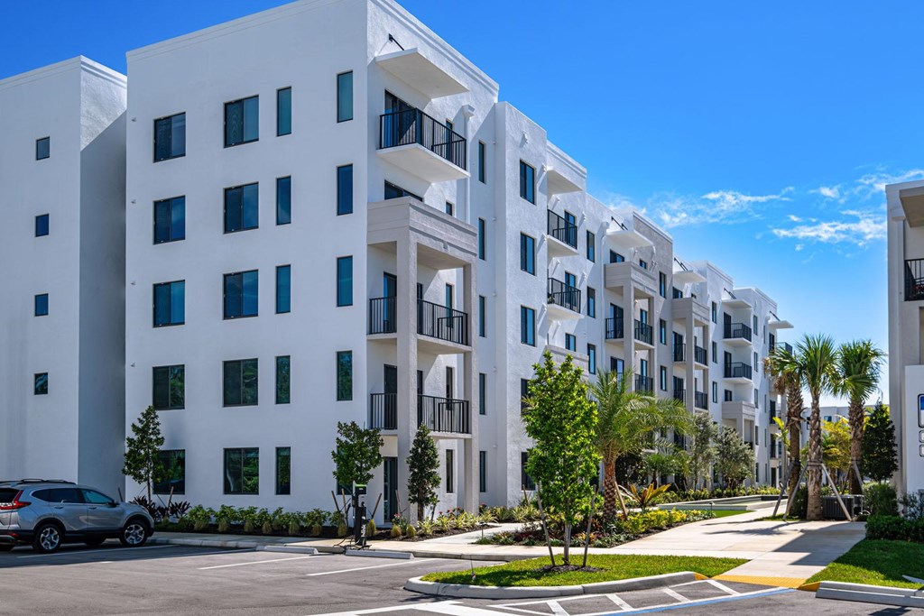 A row of white buildings with balconies and trees in front.