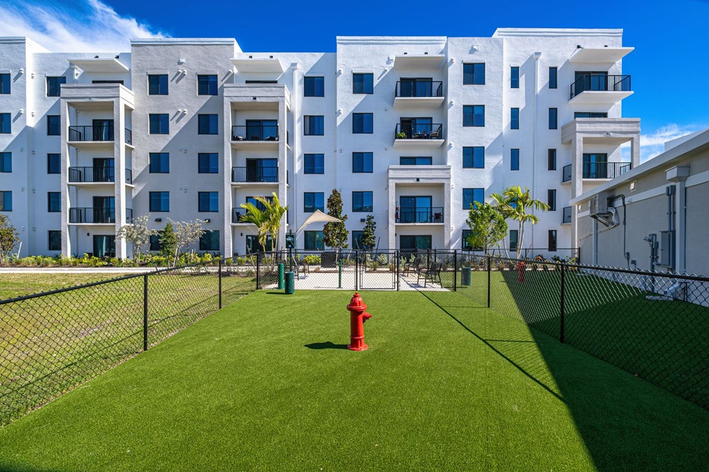 A red fire hydrant sits in the middle of a green lawn in front of a white apartment building.