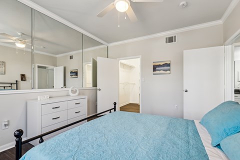 A bedroom with a blue bedspread and a large mirror above the dresser.