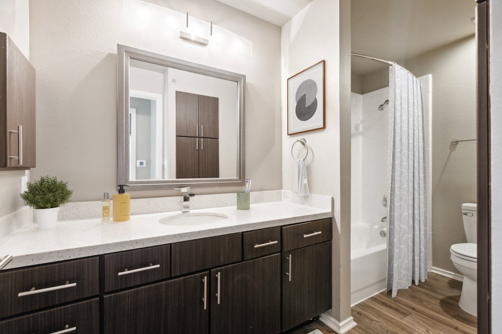 A bathroom with a white counter top and brown cabinets.