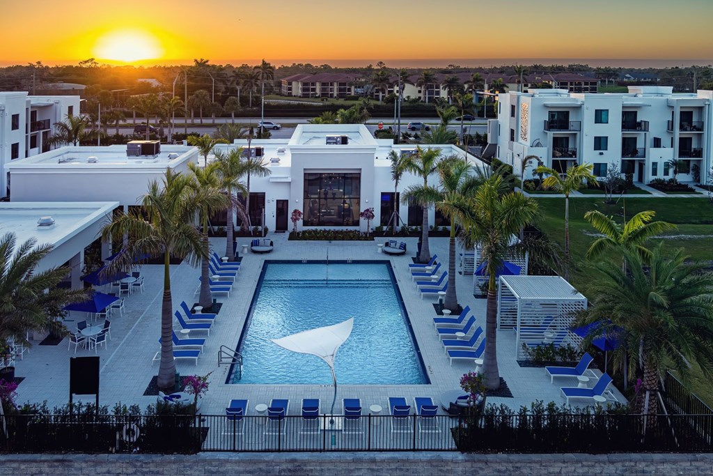 A sunset view of a pool surrounded by palm trees and apartment buildings.