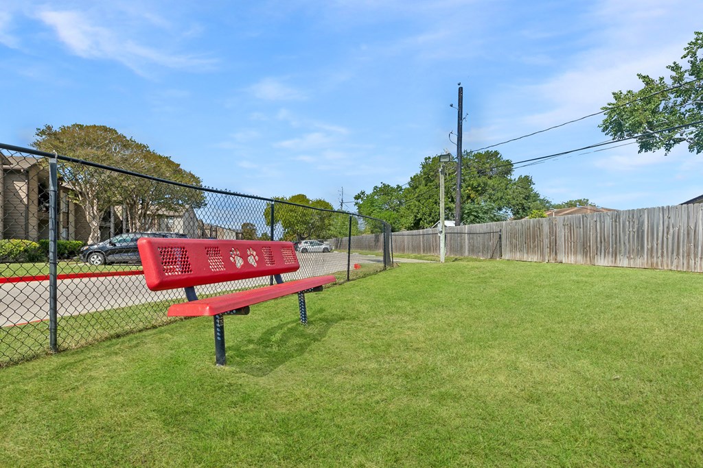 A red bench sits in a grassy area next to a fence.