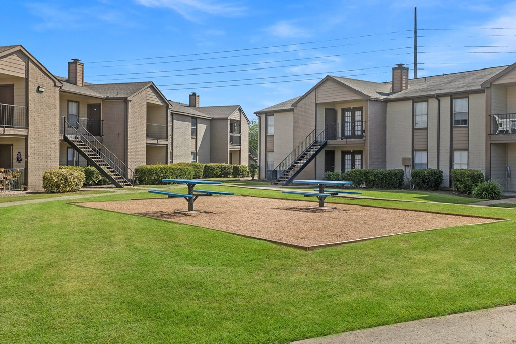 A park area with benches and a playground in front of apartment buildings.