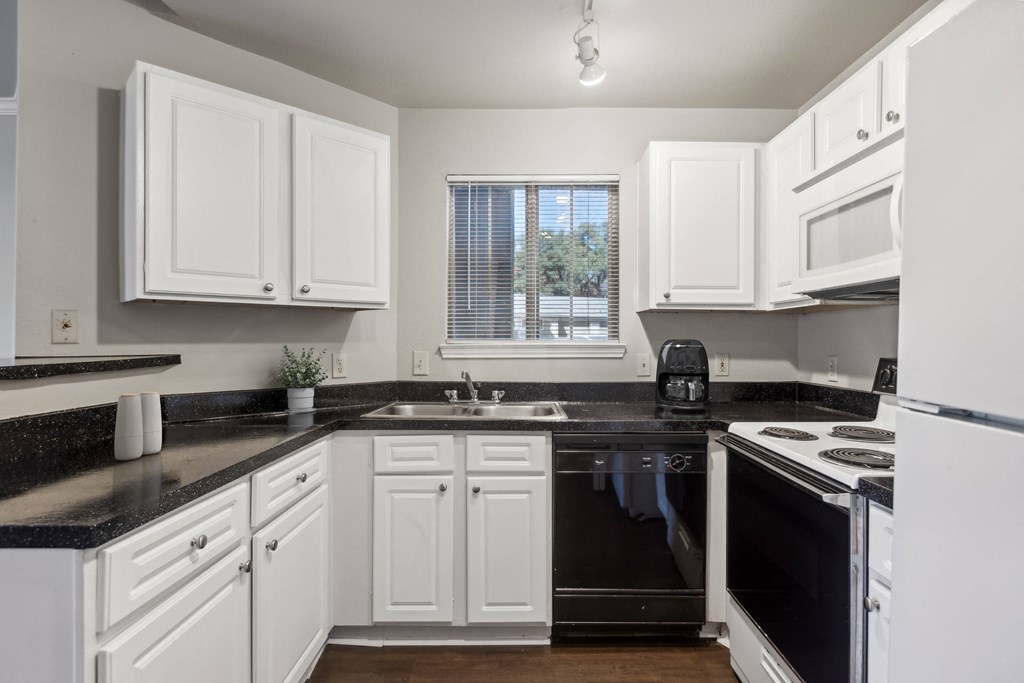 A kitchen with white cabinets and black countertops.