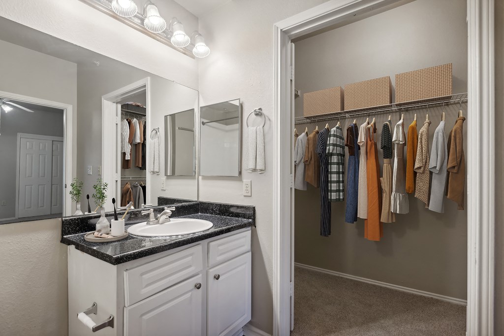A bathroom with a sink, mirror, and a closet with clothes.