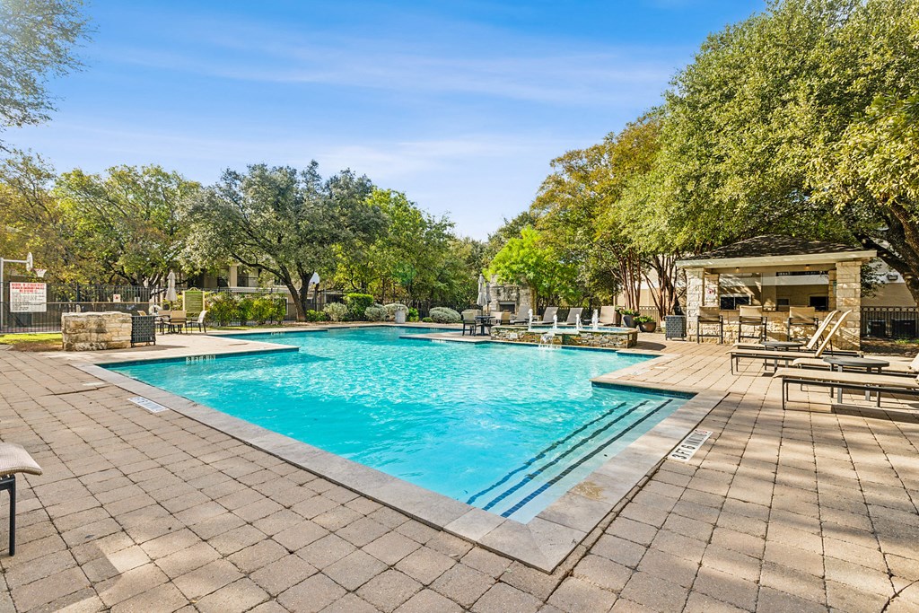 A large outdoor swimming pool surrounded by trees and a patio area with sun loungers.