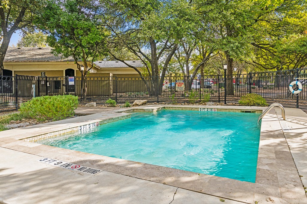 A small pool surrounded by trees and a fence.