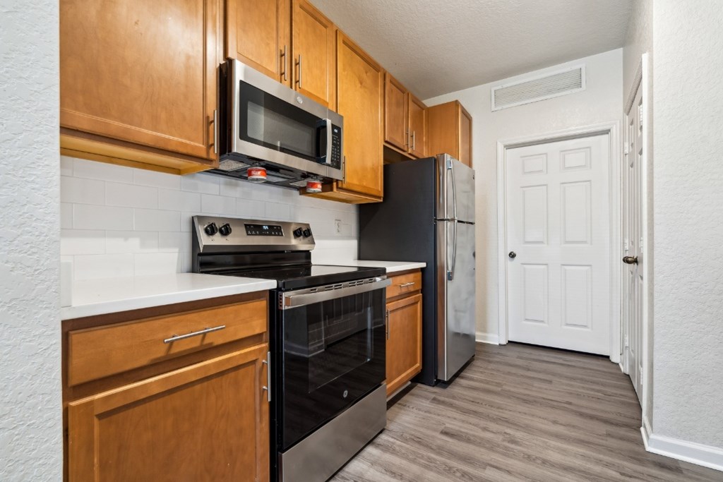 An open-concept apartment with updated lighting, stainless steel appliances, quartz countertops, vinyl plank wood style flooring and wooden cabinets.