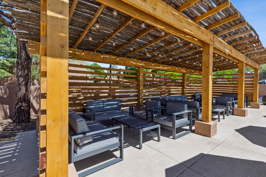 a covered patio with chairs and tables under a wooden structure  at Acacia Gardens, Albuquerque, NM
