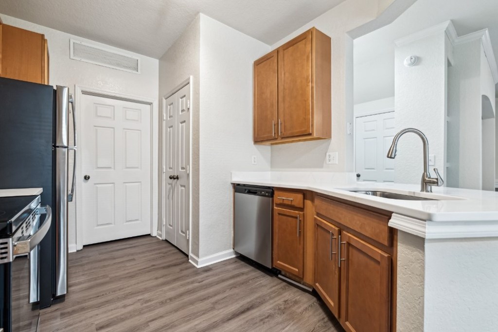 An open-concept apartment with updated lighting, stainless steel appliances, quartz countertops, vinyl plank wood style flooring and wooden cabinets.