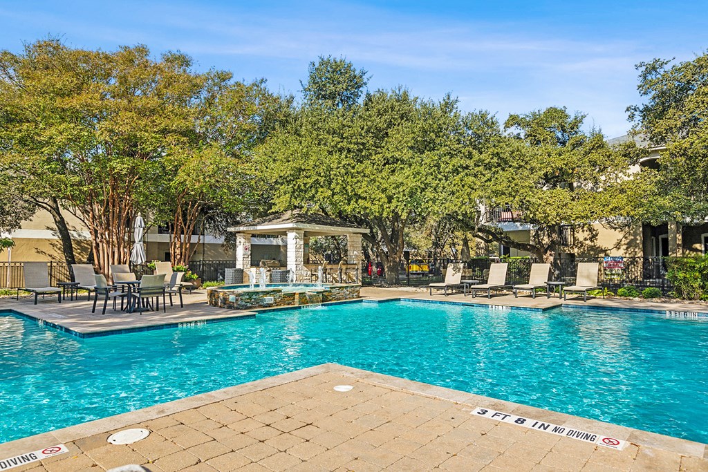 A pool surrounded by trees and chairs.