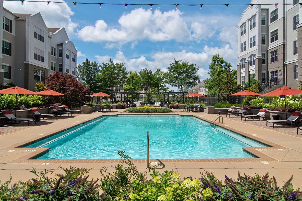 a swimming pool with lounge chairs and umbrellas in front of an apartment building at Emblem Alpharetta, Alpharetta, 30009
