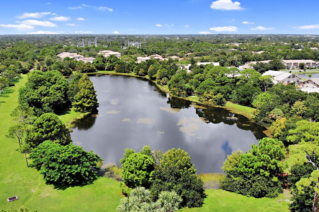 A lake surrounded by green trees and buildings in the distance.