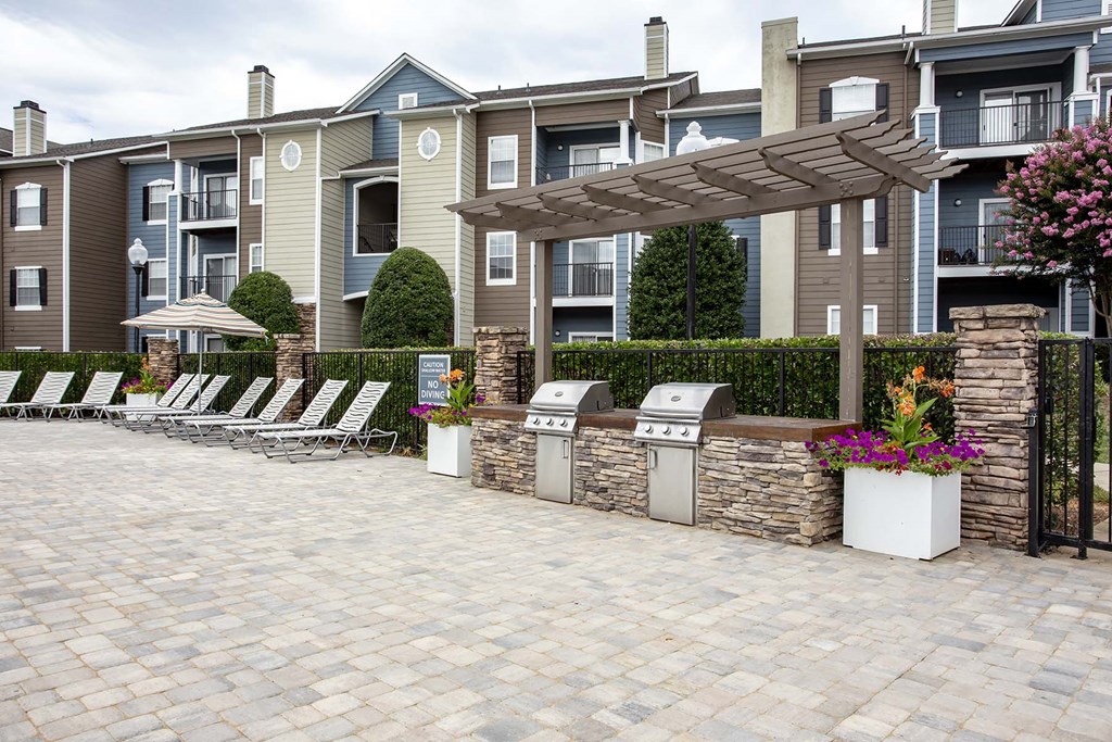 Grill Area | Thornberry Apartments a patio with chairs and a pergola in front of an apartment building at Thornberry Apartments, Charlotte, NC 28262
