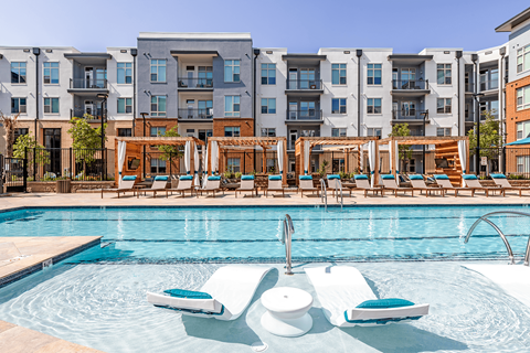 A swimming pool with lounge chairs and a fountain in the middle of it.