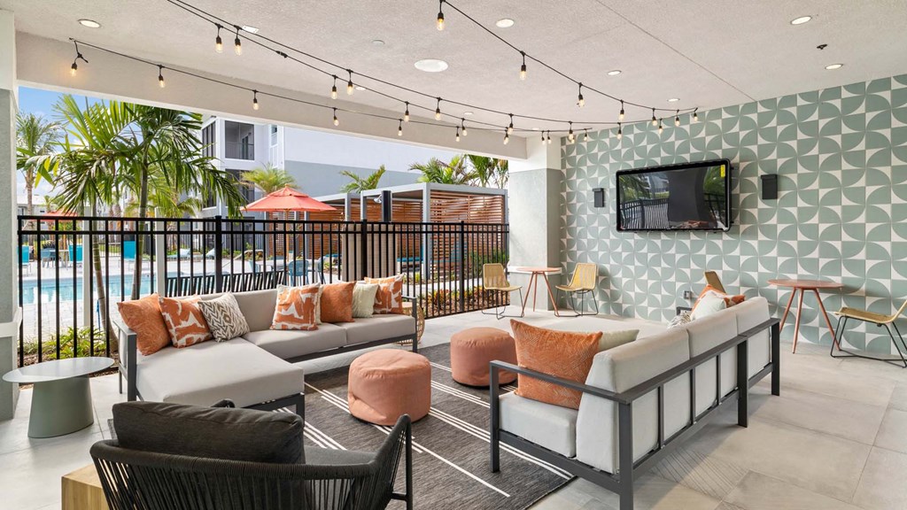 A modern outdoor seating area with a pool in the background. at Lucie at Tradition Apartments, Port St. Lucie 34987