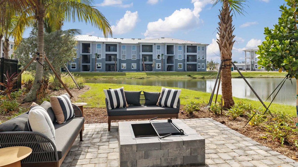 A patio with a couch, table, and chairs overlooking a pond and apartment building. at Lucie at Tradition Apartments, Florida, 34987