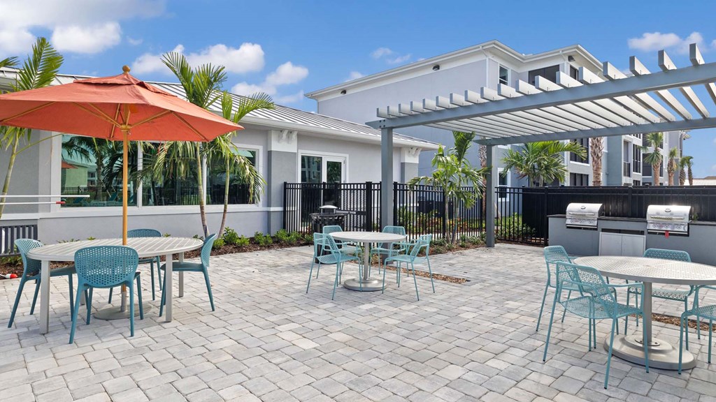 A patio with a table and chairs under a red umbrella. at Lucie at Tradition Apartments, Port St. Lucie, FL
