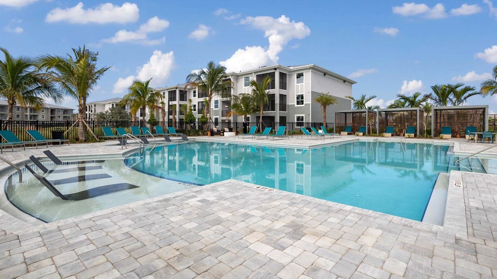 A large swimming pool surrounded by palm trees and lounge chairs. at Lucie at Tradition Apartments, Port St. Lucie, Florida