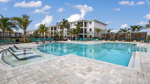 A large swimming pool surrounded by palm trees and lounge chairs. at Lucie at Tradition Apartments, Port St. Lucie, Florida