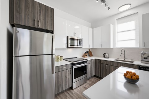 A modern kitchen with a stainless steel refrigerator and a bowl of oranges on the counter.