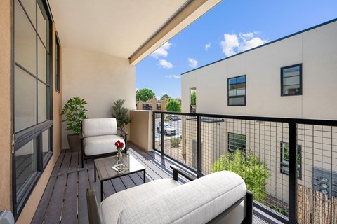 A balcony with a chair and a table with a vase of flowers on it.