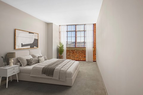 A large carpeted bedroom with exposed brick and large windows with natural light