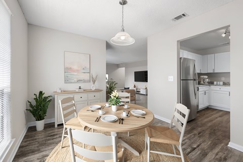 A dining room with a table set for two and a kitchen in the background.