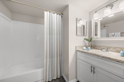 A bathroom with a white tub, sink, and striped shower curtain.
